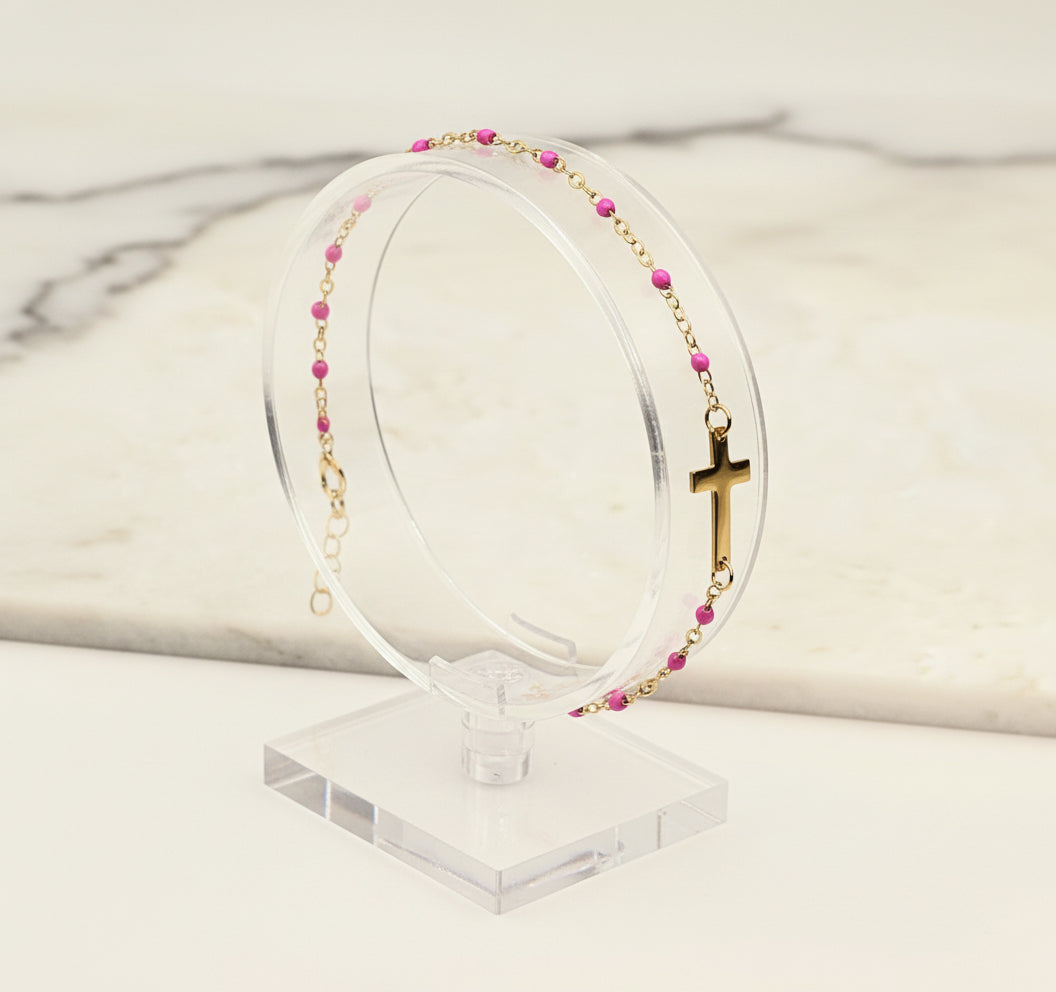 Gold bracelet with pink beads and a cross on a beige background