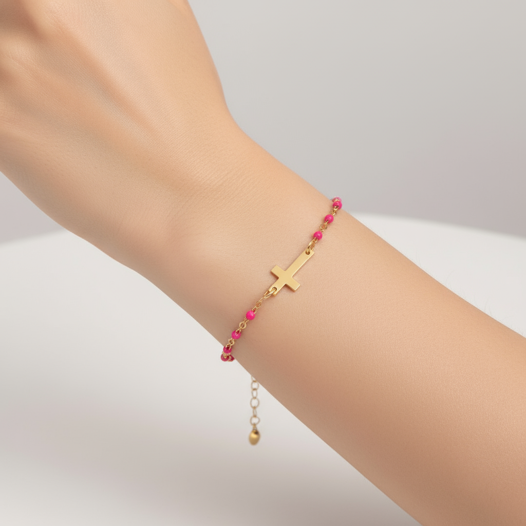 Gold bracelet with pink beads and a cross charm on a white background