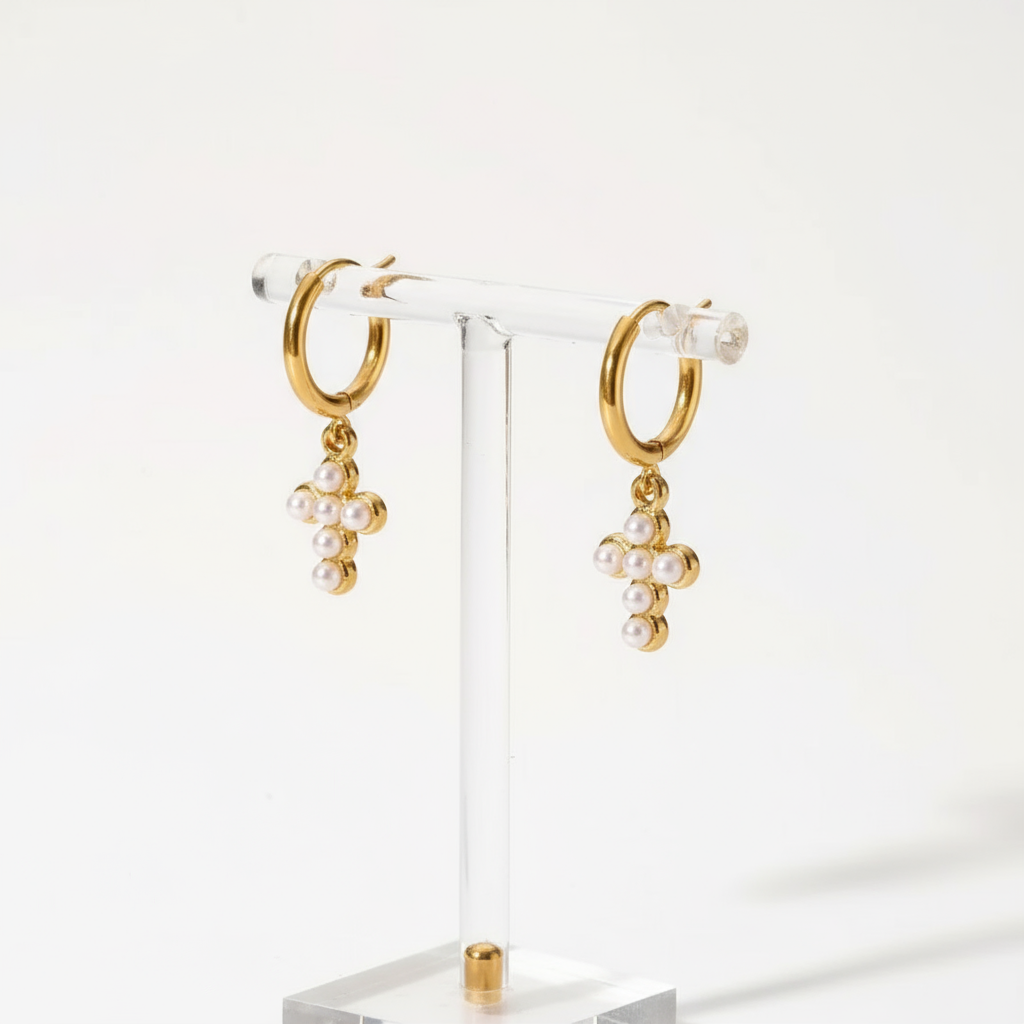 Gold hoop earrings with pearl and cross charms on a textured beige surface