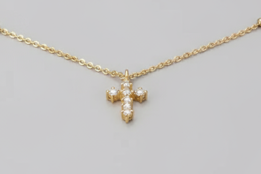 Gold necklace held by a hand with a blurred floral background