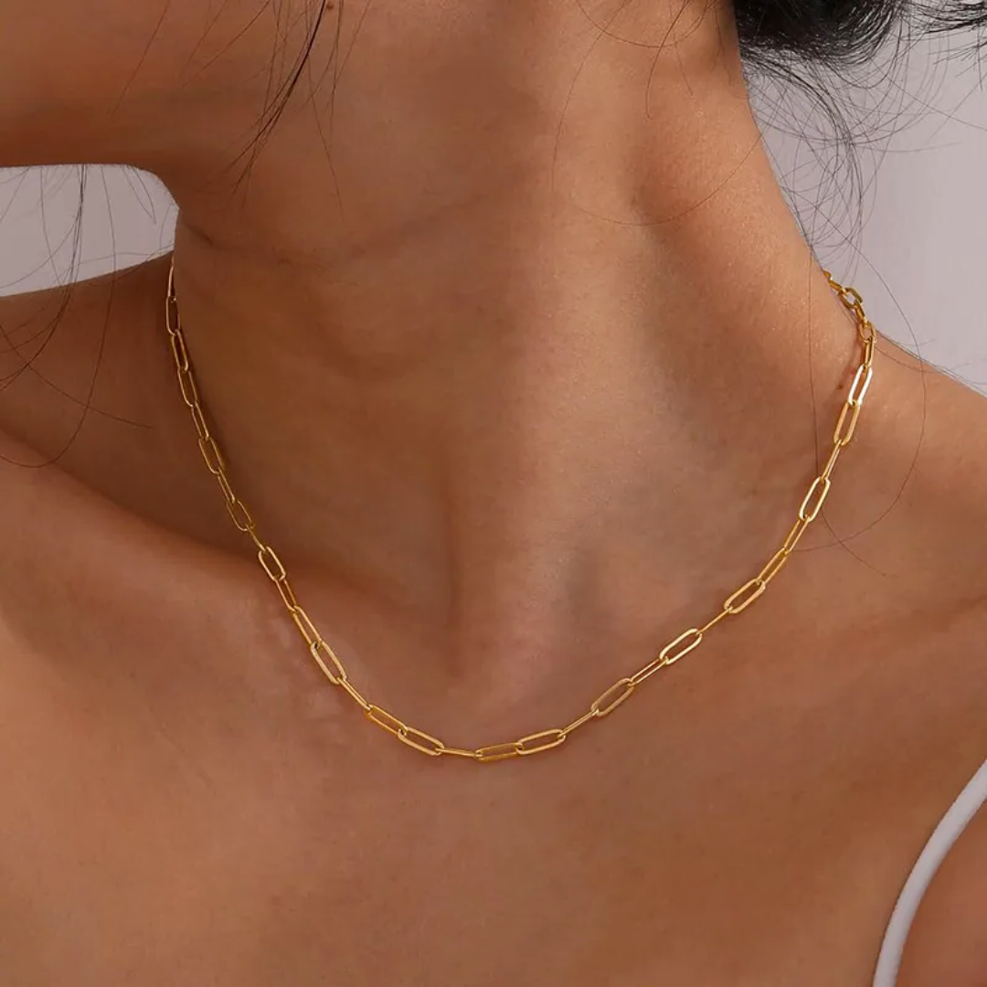 Gold chain necklace on a person's neck with a neutral background